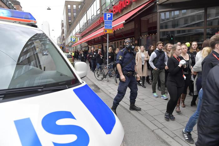 epa05894651 Swedish police officers wearing gas masks watch over people walking at a road after a truck reportedly crashed into a department store in central Stockholm, Sweden, 07 April 2017. A truck has driven into a department store on Drottninggatan street (Queen Street) in central Stockholm, media reported quoting local police. According to initial reports, at least three people were killed and others were injured in the incident, media added. Swedish Prime Minister Stefan Loefven commented that everything indicated the incident as a 'terror attack.'  EPA/JESSICA GOW  SWEDEN OUT